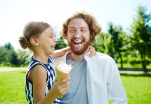 Laughing girl with ice-cream and her father having fun in park at leisure