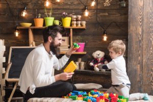 Dad and child play with toy cars, bricks. Nursery with toys and chalkboard.