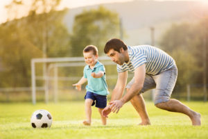 father son playing soccer in field